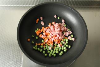 不粘锅中倒入适量玉米油，开大火烧热，倒入胡萝卜丁、香肠丁、豌豆翻炒。