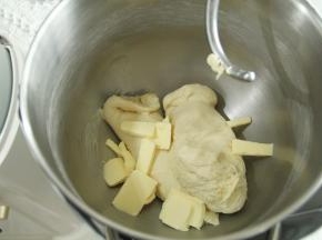 3、一档混合成团，转4-5档打至略光滑状态。轻轻扯开，粗膜状态，放入软化好的黄油。