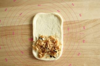 7、取一面团，按扁擀开成长方形，翻面整理。底部1/2抹上沙拉酱，放肉松。