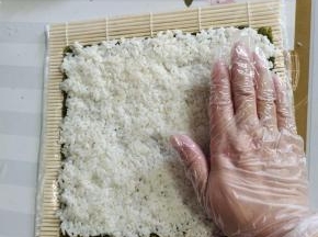 左手固定住海苔，右手手掌根部向上，按，推滑米饭！往下的时候用手指肚向下按，推滑米饭！