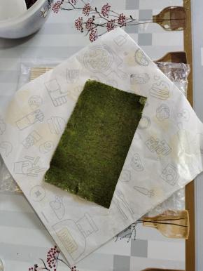 取一张台湾饭团包装纸，（饭团包装纸反面朝上，对角的方式去放！）半张寿司海苔，粗糙面朝上，斜着放在包装纸上！