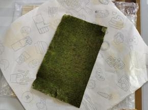 取一张台湾饭团包装纸，（饭团包装纸反面朝上，对角的方式去放！）半张寿司海苔，粗糙面朝上，斜着放在包装纸上！