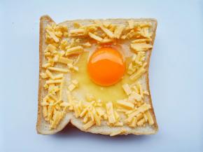 取两个常温鸡蛋，将鸡蛋打入窝窝中。在边缘摆满芝士碎。