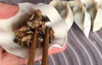 取饺子皮放在手掌上，再放入拌好的梅干菜馅