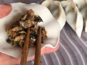取饺子皮放在手掌上，再放入拌好的梅干菜馅