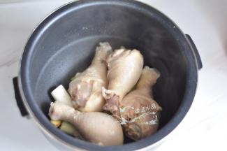 把葱段和姜片铺在电饭煲内胆底部，放入鸡腿。