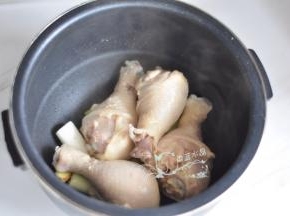 把葱段和姜片铺在电饭煲内胆底部，放入鸡腿。