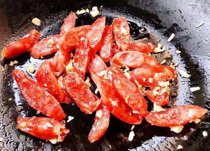 另起锅倒入底油加热放入蒜粒爆香再放入腊肠炒出香味