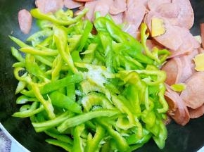 香肠拨一边，放入青椒丝和少许盐炒匀