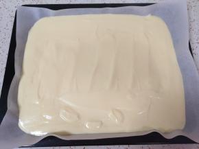 烤盘里铺上油纸，将混合好的蛋黄糊倒入烤盘，用刮铲抹平，震几下排出空气。 