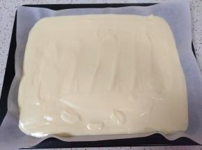 烤盘里铺上油纸，将混合好的蛋黄糊倒入烤盘，用刮铲抹平，震几下排出空气。 