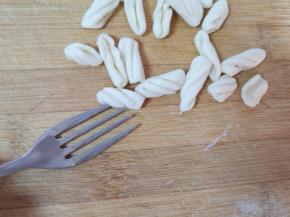 取一个叉子，将小面丁放在叉子上，用大拇指按住稍微用力顺着叉子搓下来，一个麻食就搓好了。