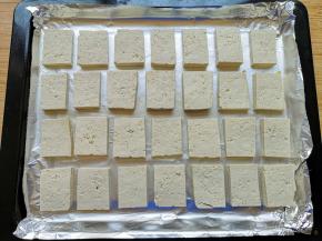 烤盘里铺上锡纸，上面刷上一层食用油，摆上切好的豆腐片，用小刀在每片豆腐上面划两刀，容易入味。 