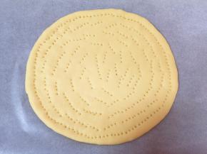 烤盘里提前铺上油纸，先取一半面团揉圆，擀成9寸大小的面片，放入烤盘，用叉子扎上小孔，防止饼皮在烤制的过程中凸起。
