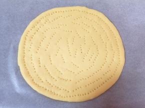 烤盘里提前铺上油纸，先取一半面团揉圆，擀成9寸大小的面片，放入烤盘，用叉子扎上小孔，防止饼皮在烤制的过程中凸起。
