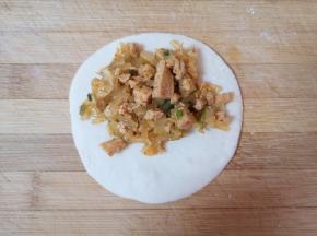 将酸菜馅放在菜盒皮一边（如图）。 