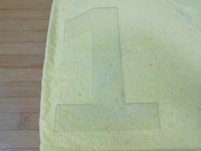 台面上铺上油纸，把蛋糕片翻过来，撕掉蛋糕片底部的油纸，放上数字模具。
