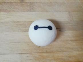 取出刚才揉好的黑色面团擀成薄片，用吸管刻出大白的眼睛，沾点水粘在包子上面，一个萌萌的大白紫薯包就做好了。