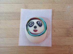 用黑色和白色的面团做出冰墩墩眼睛和鼻子，红色的的面团做出冰墩墩的嘴巴，分别沾点水粘在冰墩墩的头部。