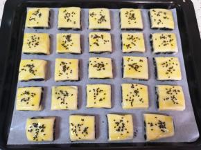 烤盘里铺上油纸，放上切好的方块酥，刷上一层蛋液，撒上熟黑芝麻。