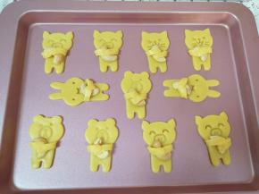 将动物饼干移至烤盘上，放上一个自己喜欢的坚果，用小动物的手臂抱起来。