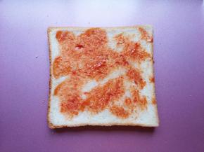 取一片吐司放在烤盘里，抹上一勺番茄酱。