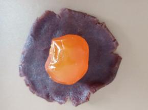 取一个豆沙按扁，包入一个蒸熟的咸蛋黄。