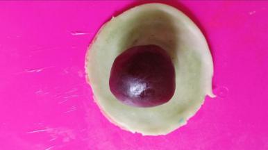 刀切的那面朝外，按扁，擀成圆形。放入一个包好的豆沙蛋黄馅。尽量用豆沙对准中间的圆心。