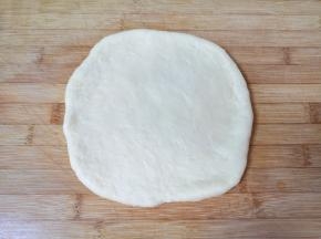 发酵好的面团揉光排气，擀成披萨盘大小的饼底。 