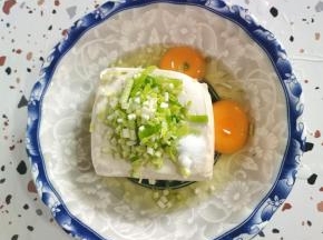 嫩豆腐放入碗中，磕入两个鸡蛋。放入适量的葱花和盐！