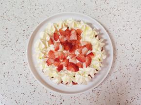 取一个大一点的盘子铺一张花边油纸，放上一片蛋糕，抹上一层奶油，放上草莓丁，用裱花袋里的奶油在蛋糕边上挤出奶油花。 