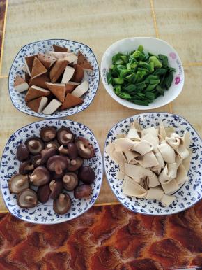 炖乌鸡的时候，我们来把自己喜欢吃的配菜处理好:
水烧开，放入一勺盐，几滴油！香菇去蒂，放进去焯水2分钟左右，捞出控干水分备用，豆干切成三角块，千张切成条，再折成蝴蝶结，蒜苗切成段备用！