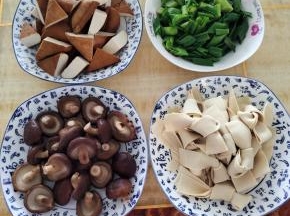 炖乌鸡的时候，我们来把自己喜欢吃的配菜处理好:
水烧开，放入一勺盐，几滴油！香菇去蒂，放进去焯水2分钟左右，捞出控干水分备用，豆干切成三角块，千张切成条，再折成蝴蝶结，蒜苗切成段备用！