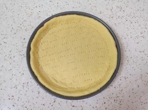 擀成比烤盘大一点的饼底，放入烤盘，用叉子扎上小孔。 