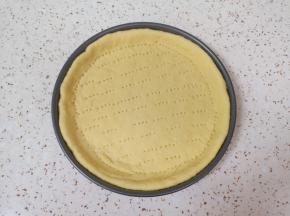 擀成比烤盘大一点的饼底，放入烤盘，用叉子扎上小孔。 