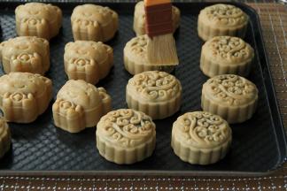 烤好取出，风炉转165度，继续预热。月饼放到手温，用羊毛刷蘸取蛋液，在碗边刮干净（新手可以把蘸好蛋液的毛刷放在油纸上，用刮板轻轻刮一下，刮去多余的蛋液），然后快速的在月饼表面刷上蛋液，刷1-2下，一定要薄。