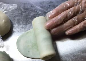 取第一个包好的面团，按压成饼，用擀面杖擀成长条，再卷成卷