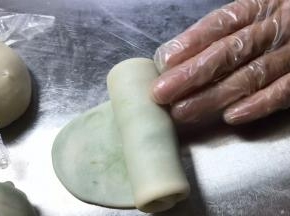 取第一个包好的面团，按压成饼，用擀面杖擀成长条，再卷成卷