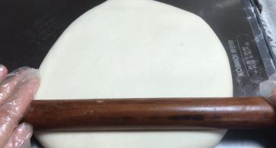 倒扣在案板上，用擀面杖轻轻按压成饼，再慢慢擀成长方形面皮