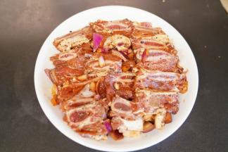 把腌制好的紫洋葱放入土豆上面，最后放入牛仔骨，把腌制的汤汁也淋入盘中