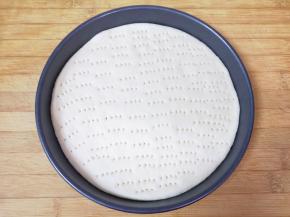 留出来三分之一的面团，剩下三分之二的面团擀成披萨盘大小的饼底，放入披萨盘，用叉子扎上小孔。