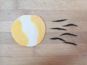 取一个小剂子用手压扁，擀成饺子皮，取一点黑色的面团搓成两头尖的小条条，如图。