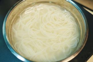 把煮好的过桥米线倒入滤水盆里，用清水冲一下