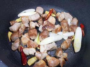 下入葱段、干红辣椒和花椒，翻炒至羊肉微微出油。