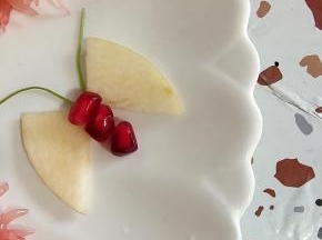 一片苹果对半切开，再对着摆放，中间放3颗石榴点缀一下，用香菜梗当蝴蝶的胡须！一只蝴蝶就做好了！