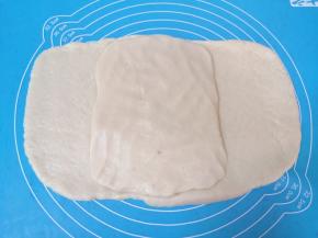 将油酥面团压成长方形，放在油皮面团中间（如图）。