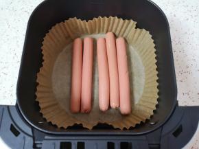 空气炸锅炸篮里铺上专用油纸，放入火腿肠，刷上一层调和油。