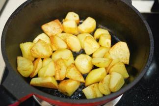 热锅后倒入植物油，放入去皮滚刀切块的土豆煎炒至表面金黄