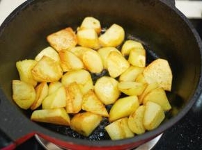 热锅后倒入植物油，放入去皮滚刀切块的土豆煎炒至表面金黄