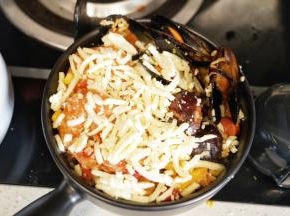 把炒好的海鲜饭放入烤碗里，在米饭上面撒入马苏里拉奶酪